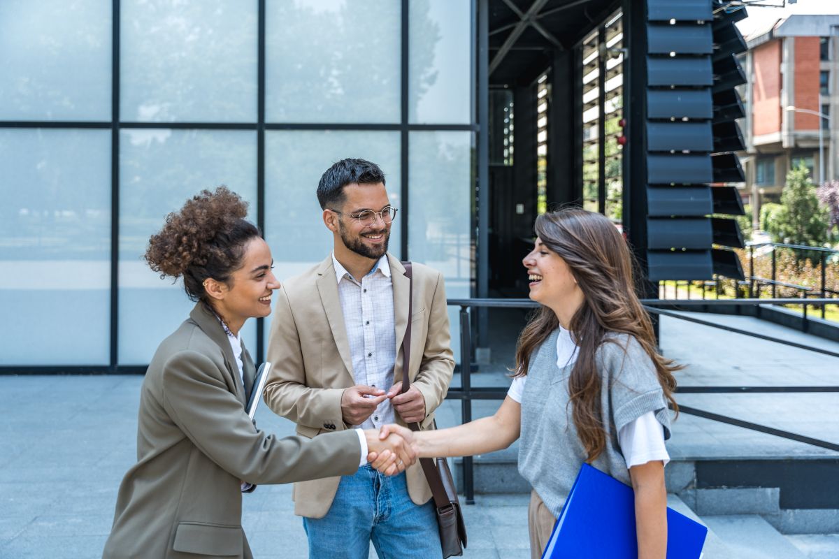 Three people with two shaking hands and smiling